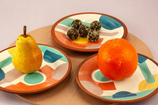 Vibrant ceramic plates featuring fresh pear, orange, and chocolate truffles on a wooden tray.